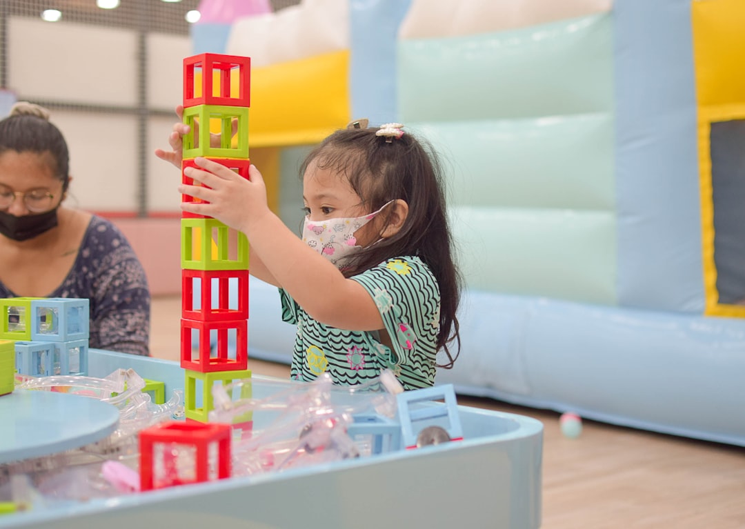 “Little girl playing with colorful building blocks in a play area, developing creativity and motor skills through imaginative play.”